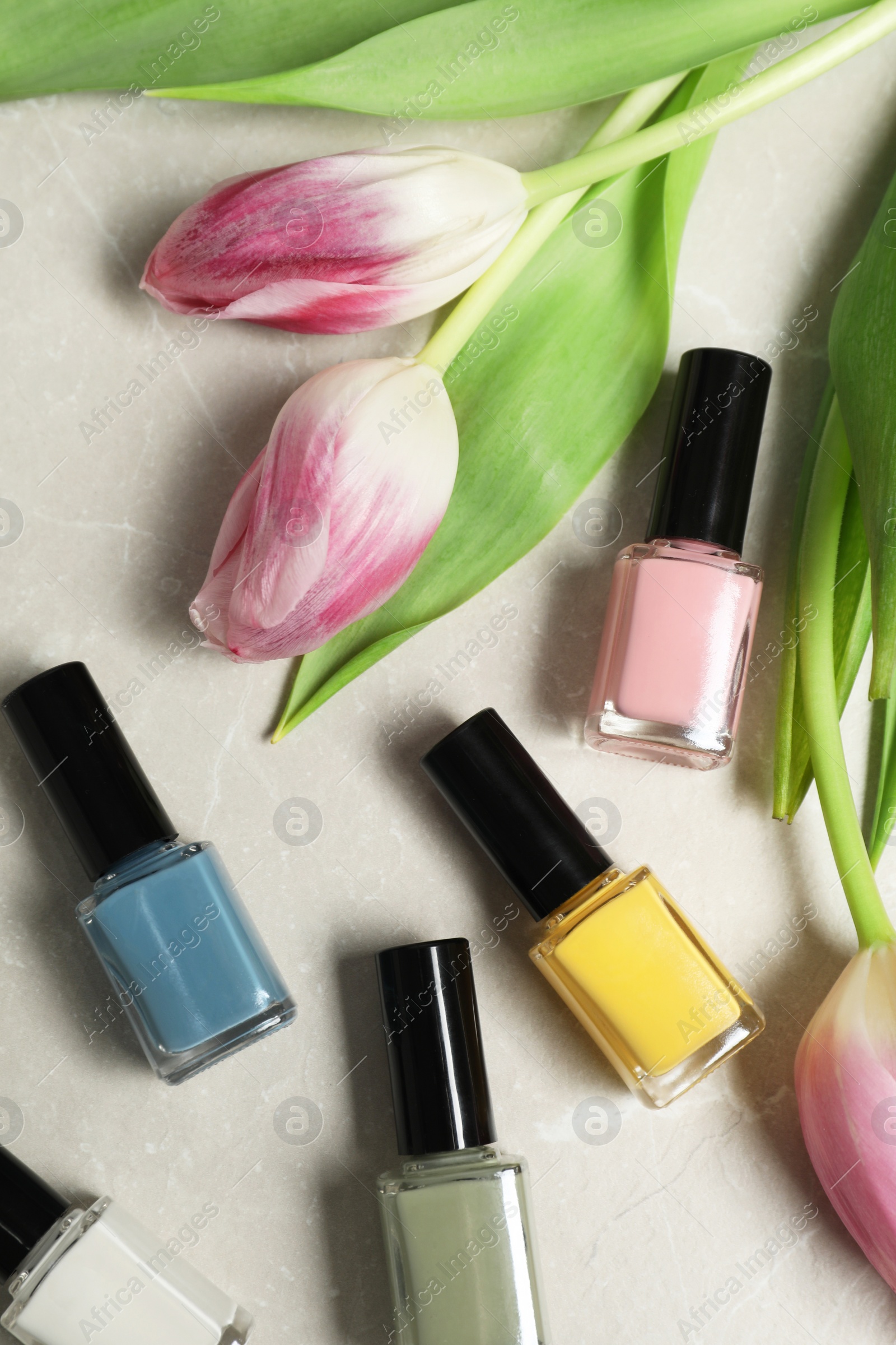 Photo of Flat lay composition with bright nail polishes in bottles and tulip flowers on light textured table