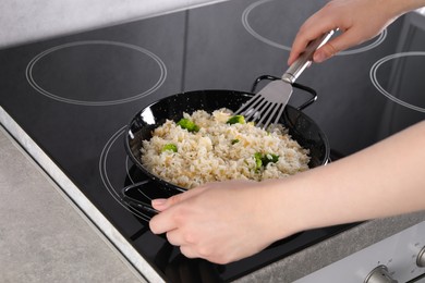 Woman frying rice with vegetables at induction stove in kitchen, closeup
