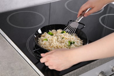 Photo of Woman frying rice with vegetables at induction stove in kitchen, closeup