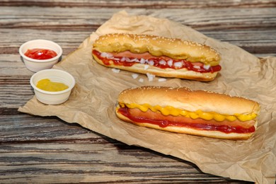 Fresh delicious hot dogs and sauces on wooden surface