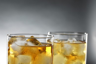 Tasty whiskey with ice in glasses on grey background, closeup