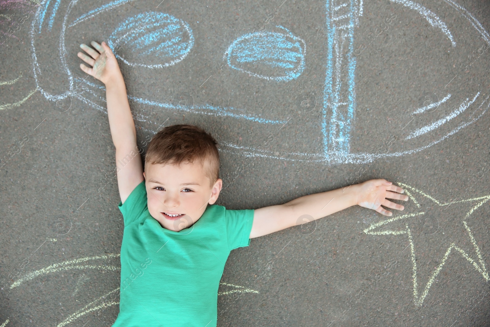 Photo of Little child lying near chalk drawing of rocket on asphalt, top view