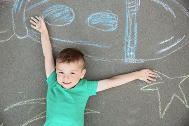 Little child lying near chalk drawing of rocket on asphalt, top view