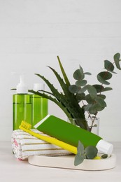 Tube of toothpaste, toothbrush, fresh aloe, eucalyptus and care products on white wooden table