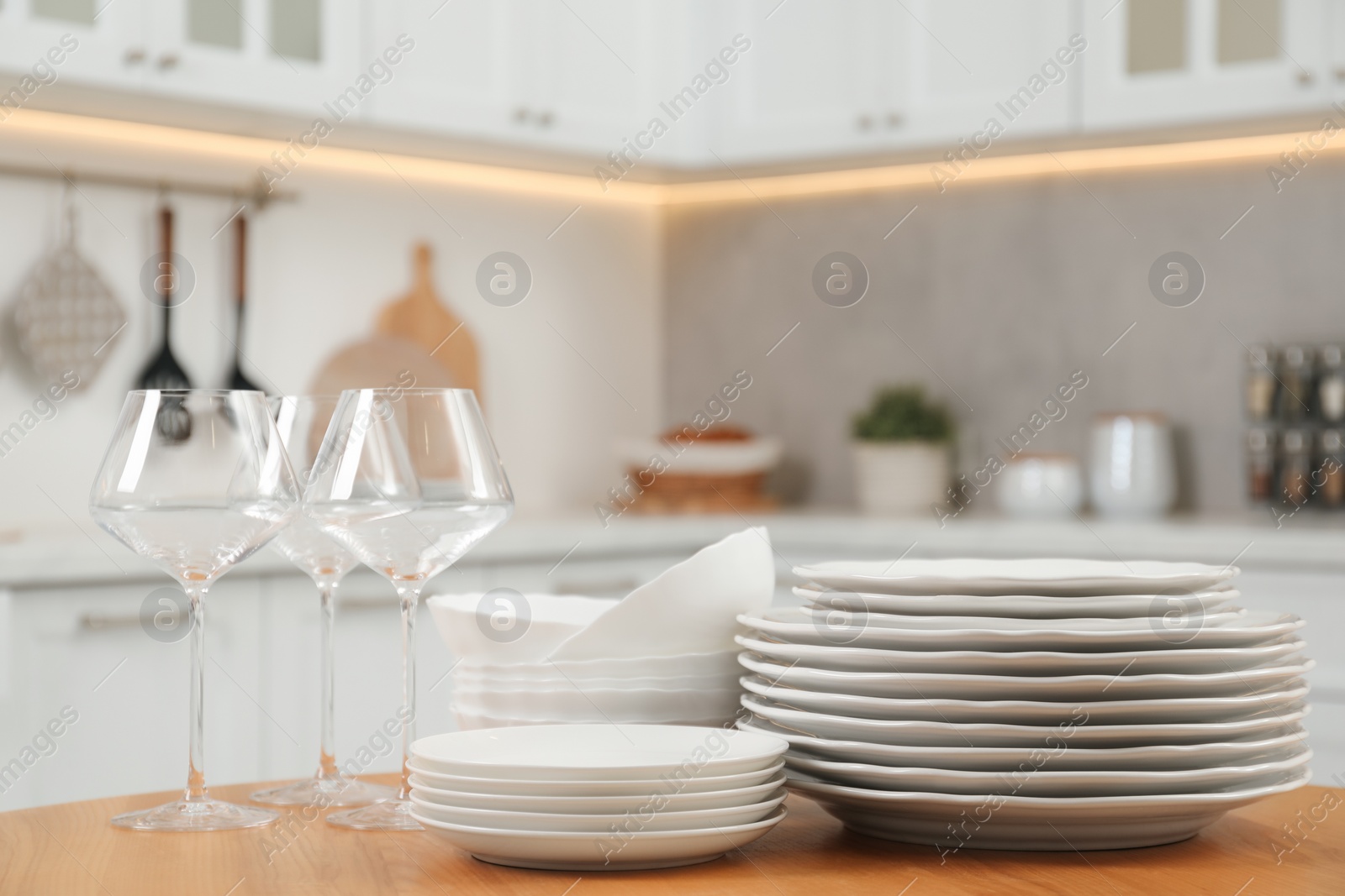 Photo of Clean plates, bowls and glasses on wooden table in kitchen