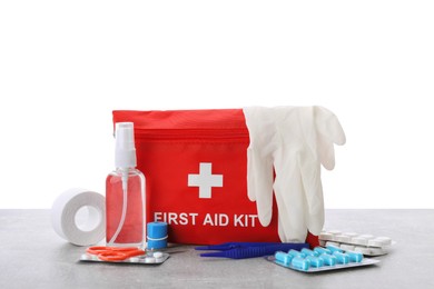 Photo of First aid kit, scissors, gloves, pills, plastic forceps and elastic bandage on light grey table against white background
