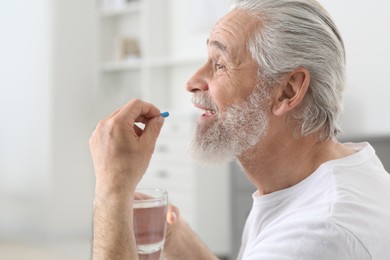 Senior man with glass of water taking pill indoors
