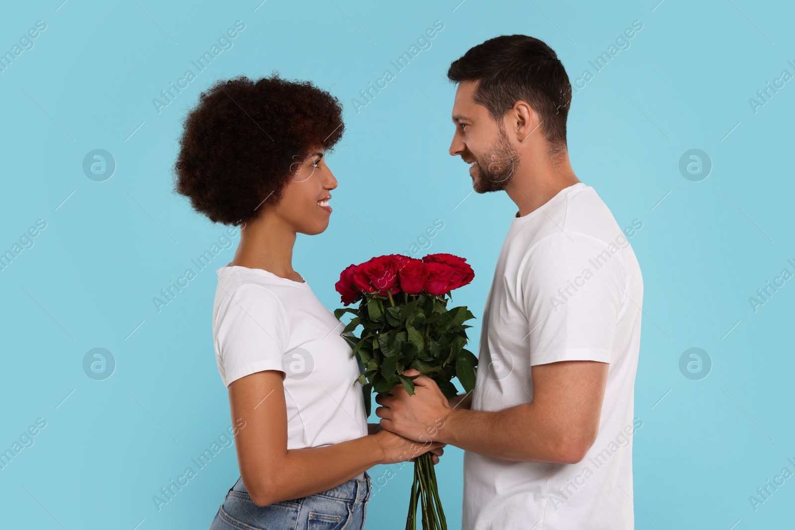 Photo of International dating. Happy couple with bouquet of roses on light blue background