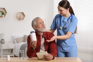 Photo of Young healthcare worker consulting senior man at wooden table indoors