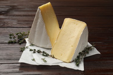 Photo of Pieces of tasty camembert cheese and thyme on wooden table, closeup