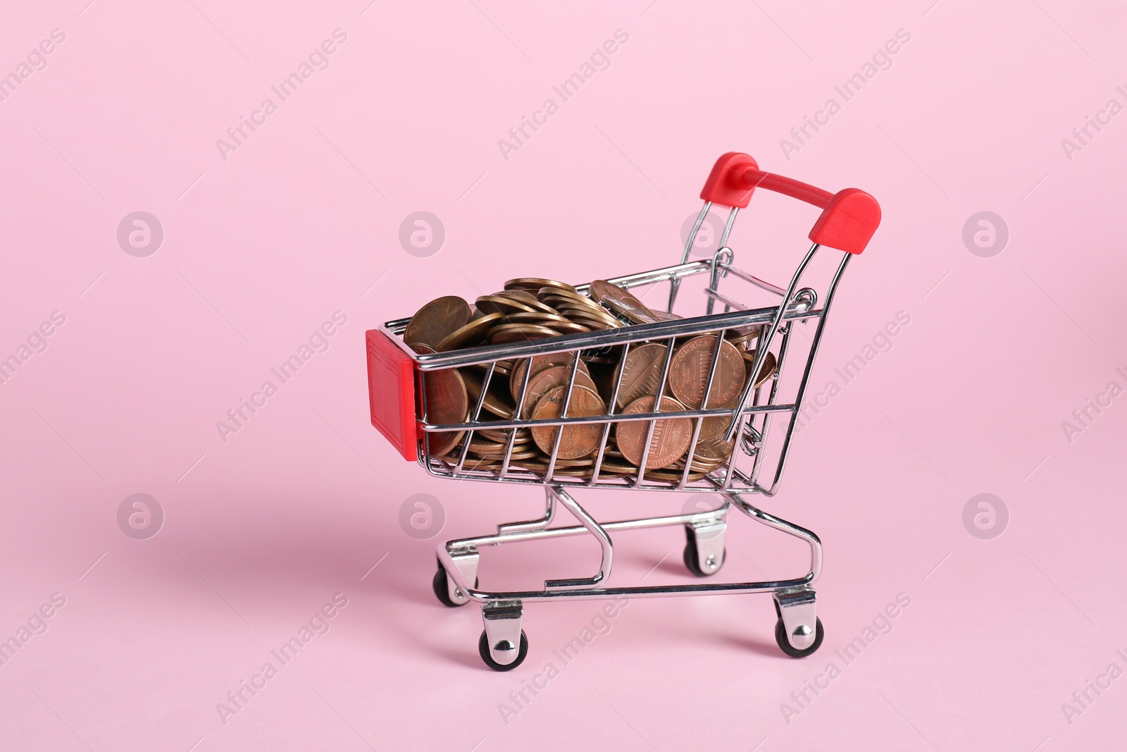 Photo of Small metal shopping cart with coins on pink background