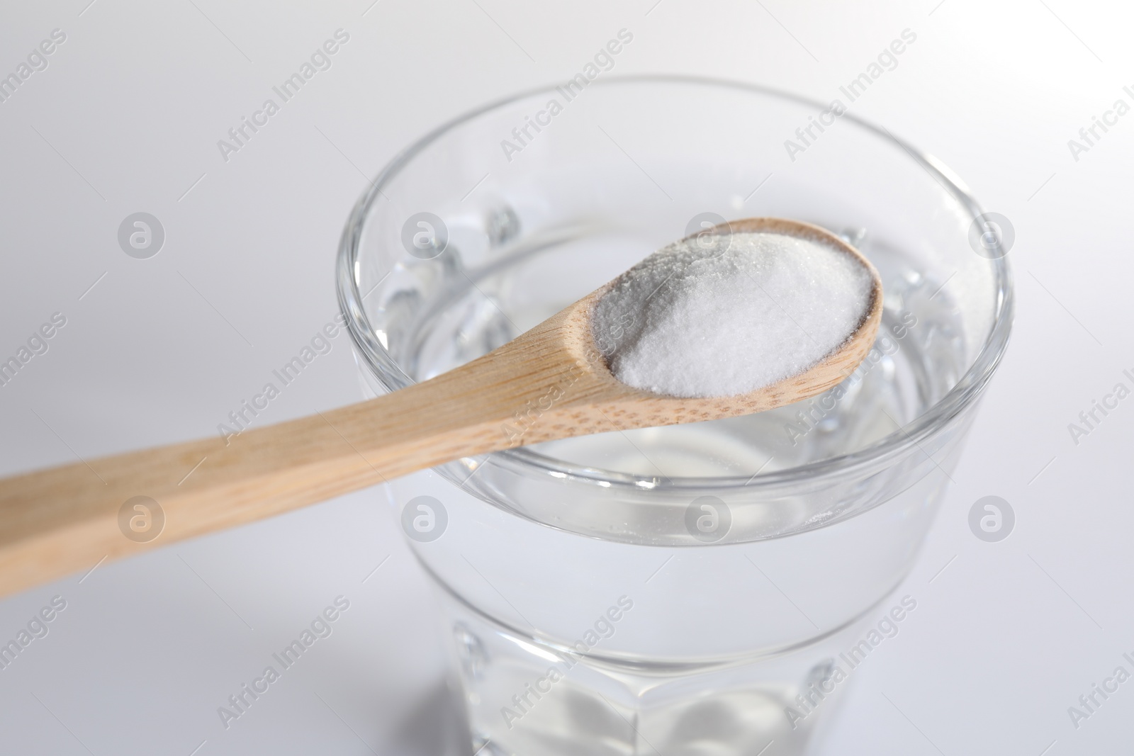 Photo of Spoon with baking soda over glass of water on white background, closeup