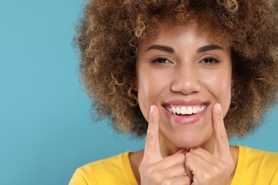 Woman showing her clean teeth and smiling on light blue background, space for text