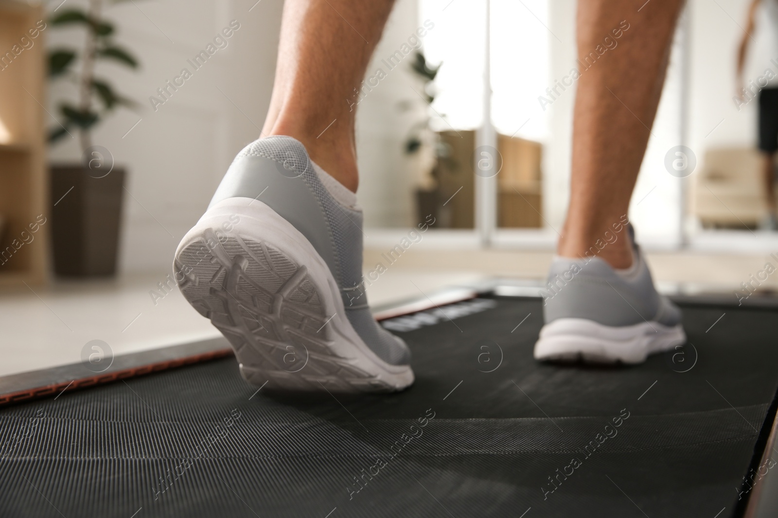 Photo of Sporty man training on walking treadmill at home, closeup