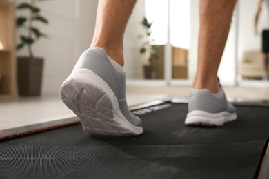 Sporty man training on walking treadmill at home, closeup