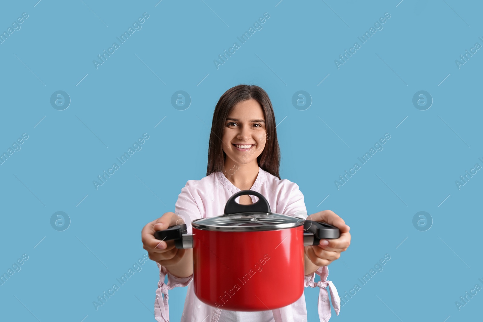 Photo of Happy young woman with cooking pot on light blue background