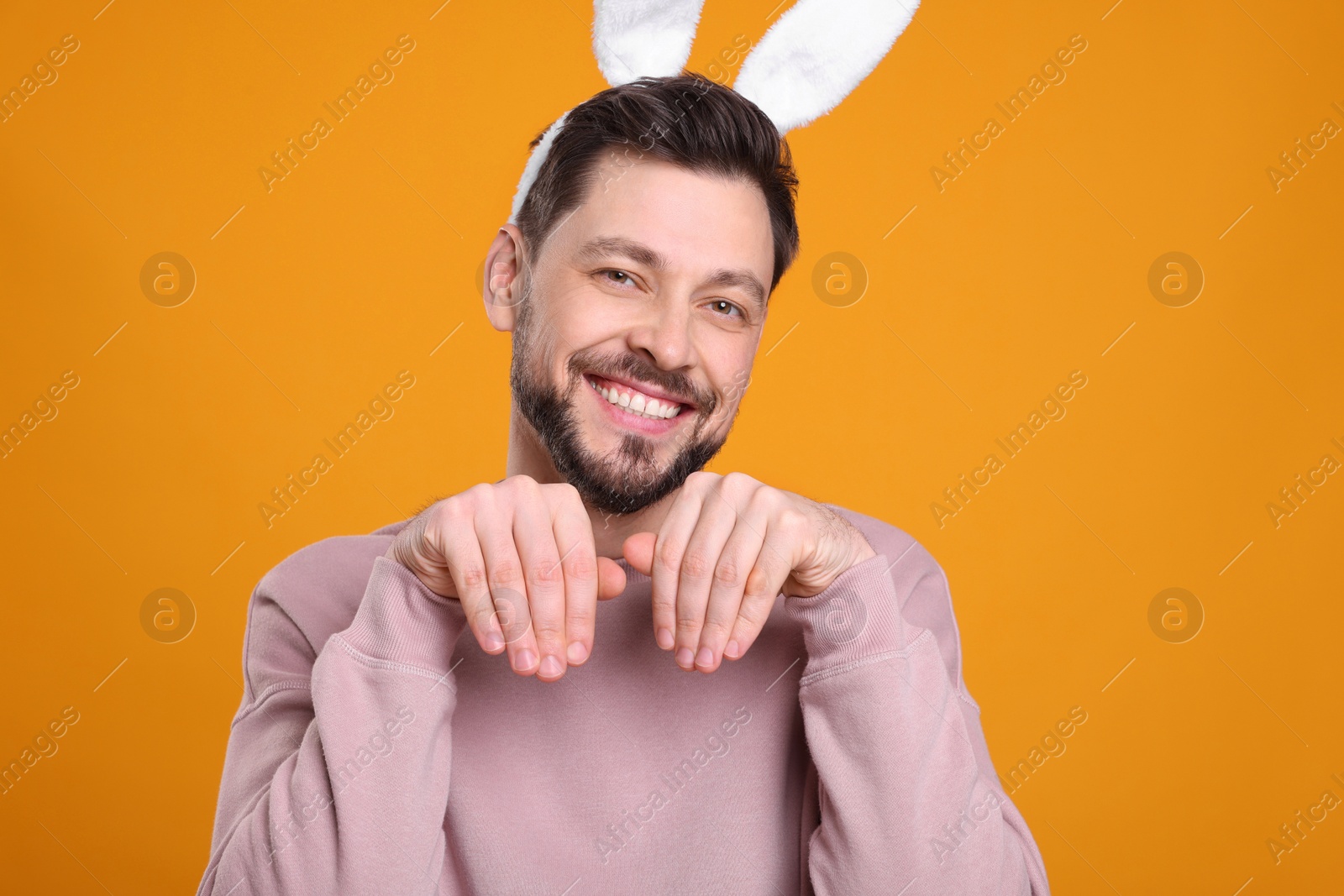Photo of Happy man wearing bunny ears headband on orange background. Easter celebration