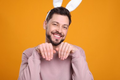 Happy man wearing bunny ears headband on orange background. Easter celebration