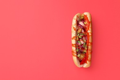 Photo of Tasty hot dog with onion, tomato, pickles and sauce on red background, top view. Space for text