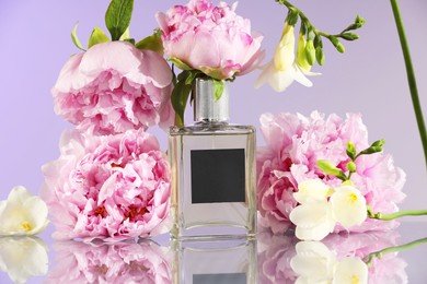 Photo of Bottle of luxury perfume and floral decor on mirror surface against light purple background