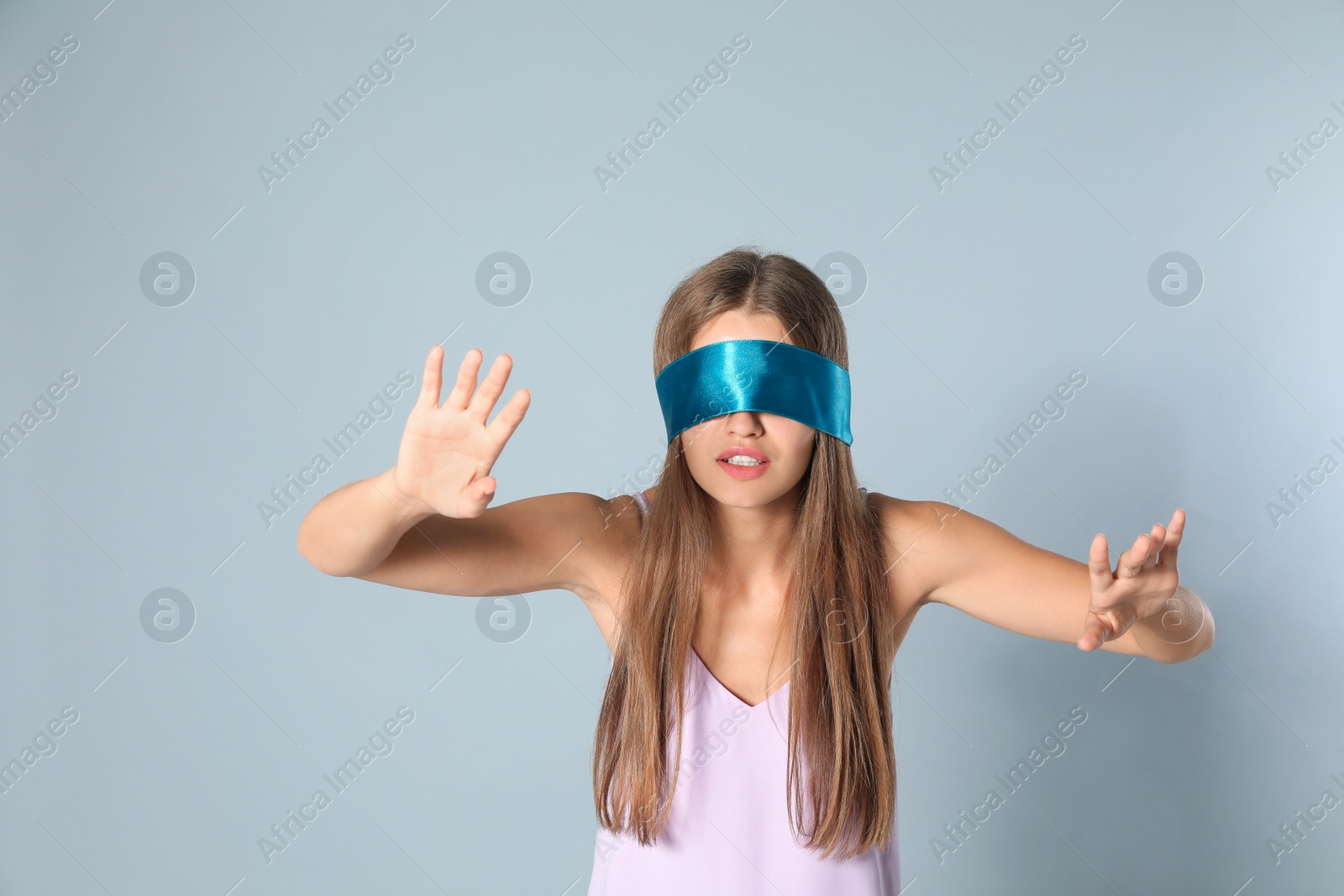 Photo of Young woman with light blue blindfold on grey background