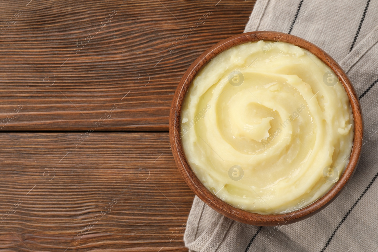 Photo of Bowl of tasty mashed potato on wooden table, top view. Space for text