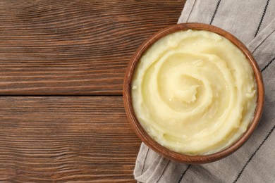 Photo of Bowl of tasty mashed potato on wooden table, top view. Space for text