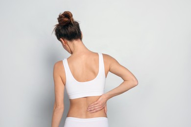 Woman suffering from pain in back on light grey background