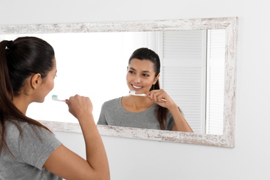 Photo of Young woman cleaning teeth against mirror in bathroom