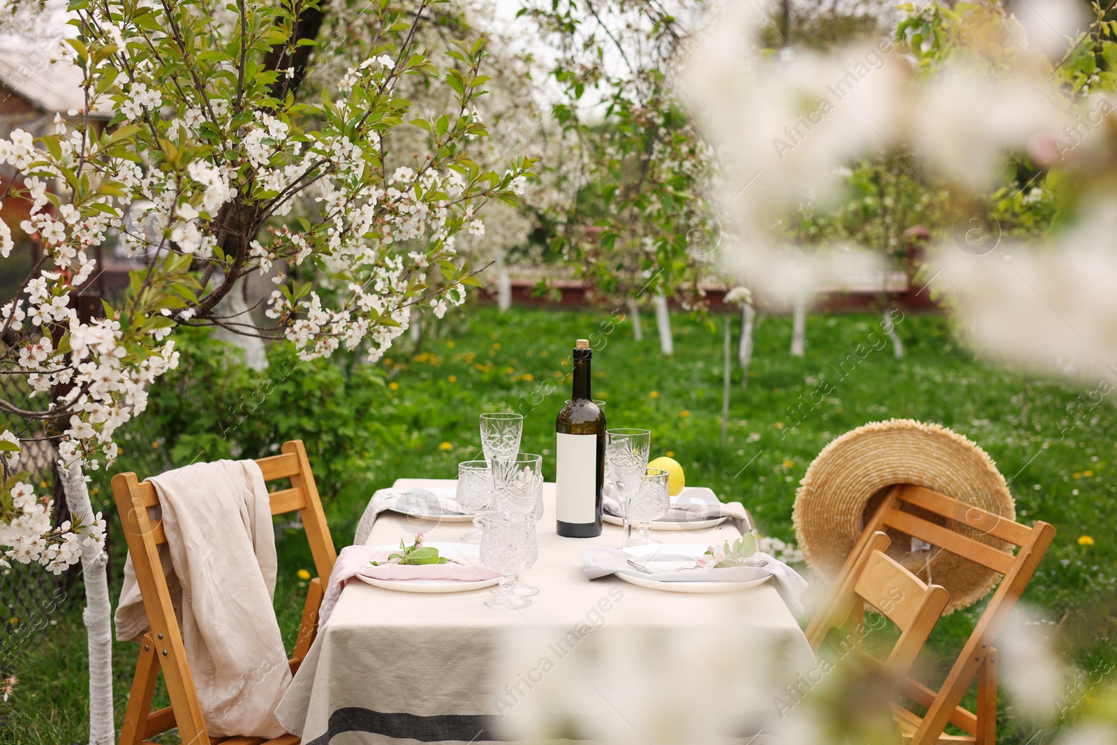 Photo of Stylish table setting with beautiful spring flowers, wine, plates and glasses in garden