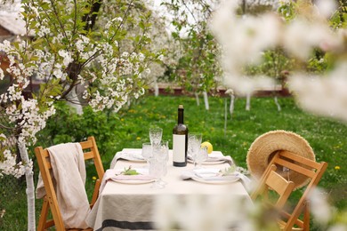 Stylish table setting with beautiful spring flowers, wine, plates and glasses in garden