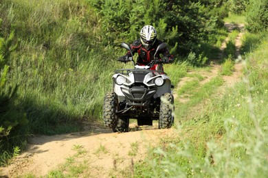 Man driving modern quad bike on sandy road near forest. Extreme sport