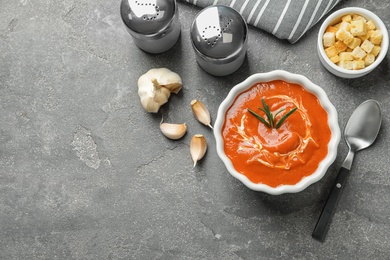 Photo of Fresh homemade tomato soup served with croutons and garlic on grey table, top view. Space for text