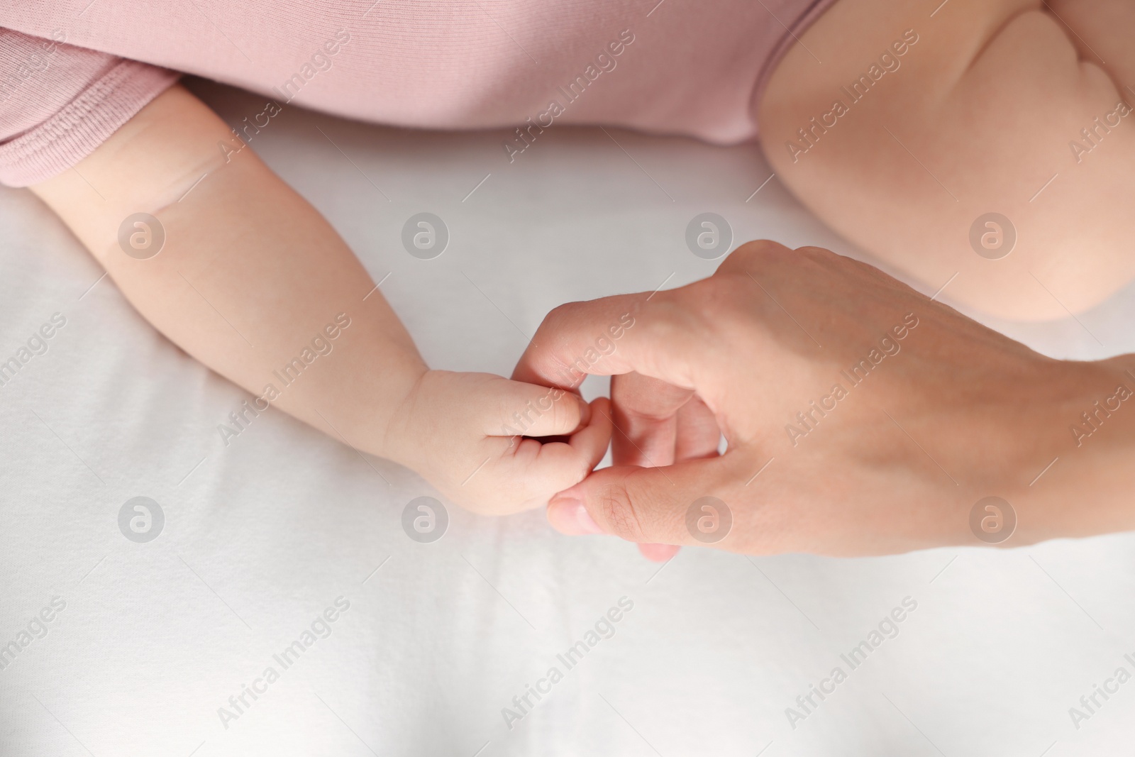 Photo of Mother holding hand of her little baby on bed, closeup