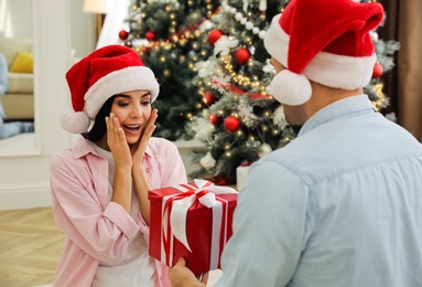 Photo of Happy couple in Santa hats with Christmas gift at home