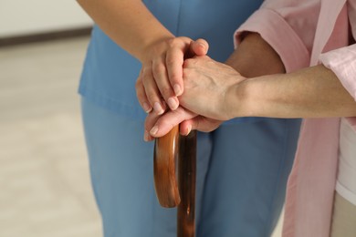 Elderly woman with walking cane and female caregiver indoors, closeup