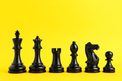 Photo of Black chess pieces on yellow background. Space for text