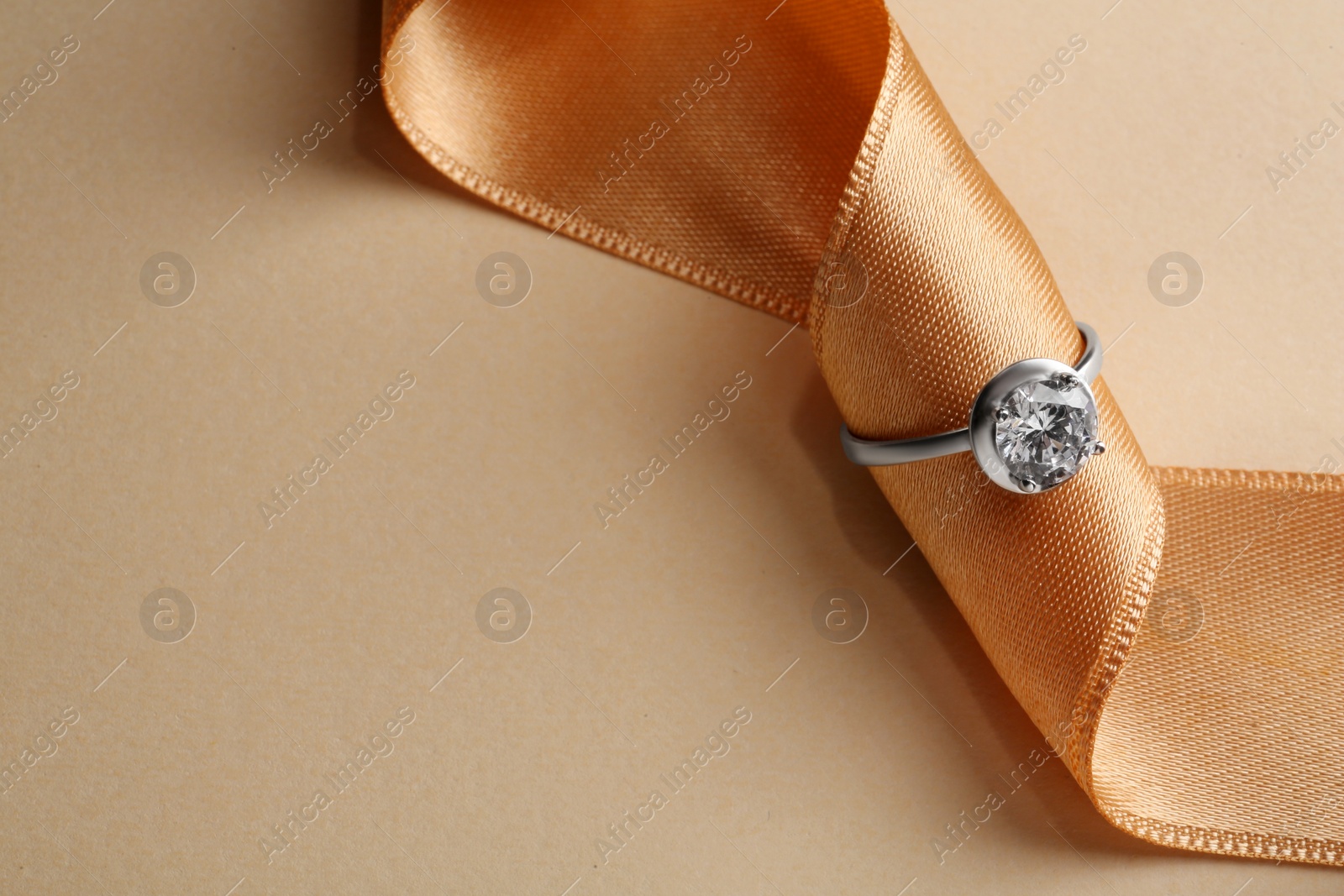 Photo of Beautiful luxury engagement ring with gemstone and ribbon on beige background, closeup. Space for text