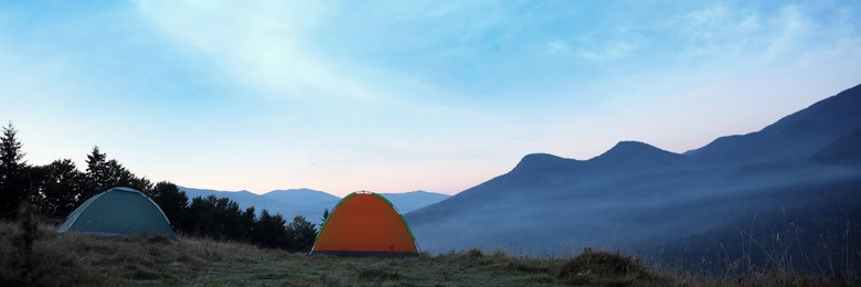 Image of Camping tents on mountain slope in morning, banner design