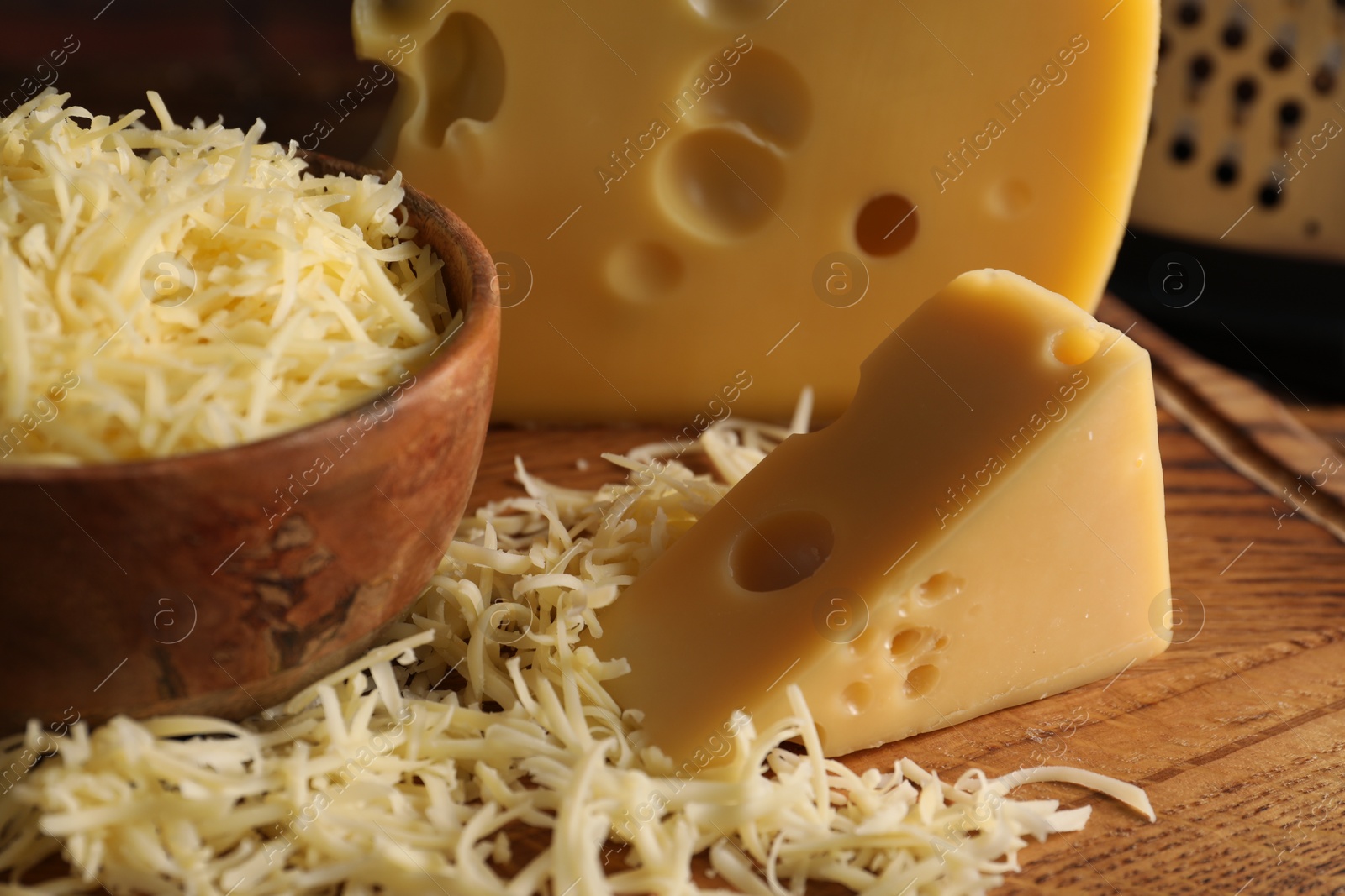 Photo of Grated and cut cheese on wooden board, closeup