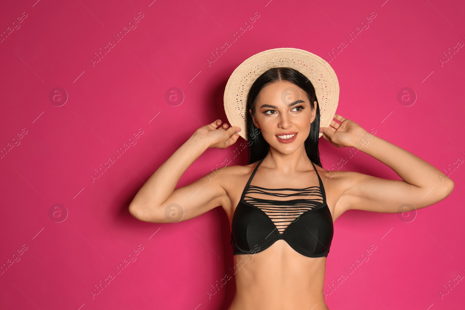 Photo of Beautiful young woman in black bikini with hat on pink background