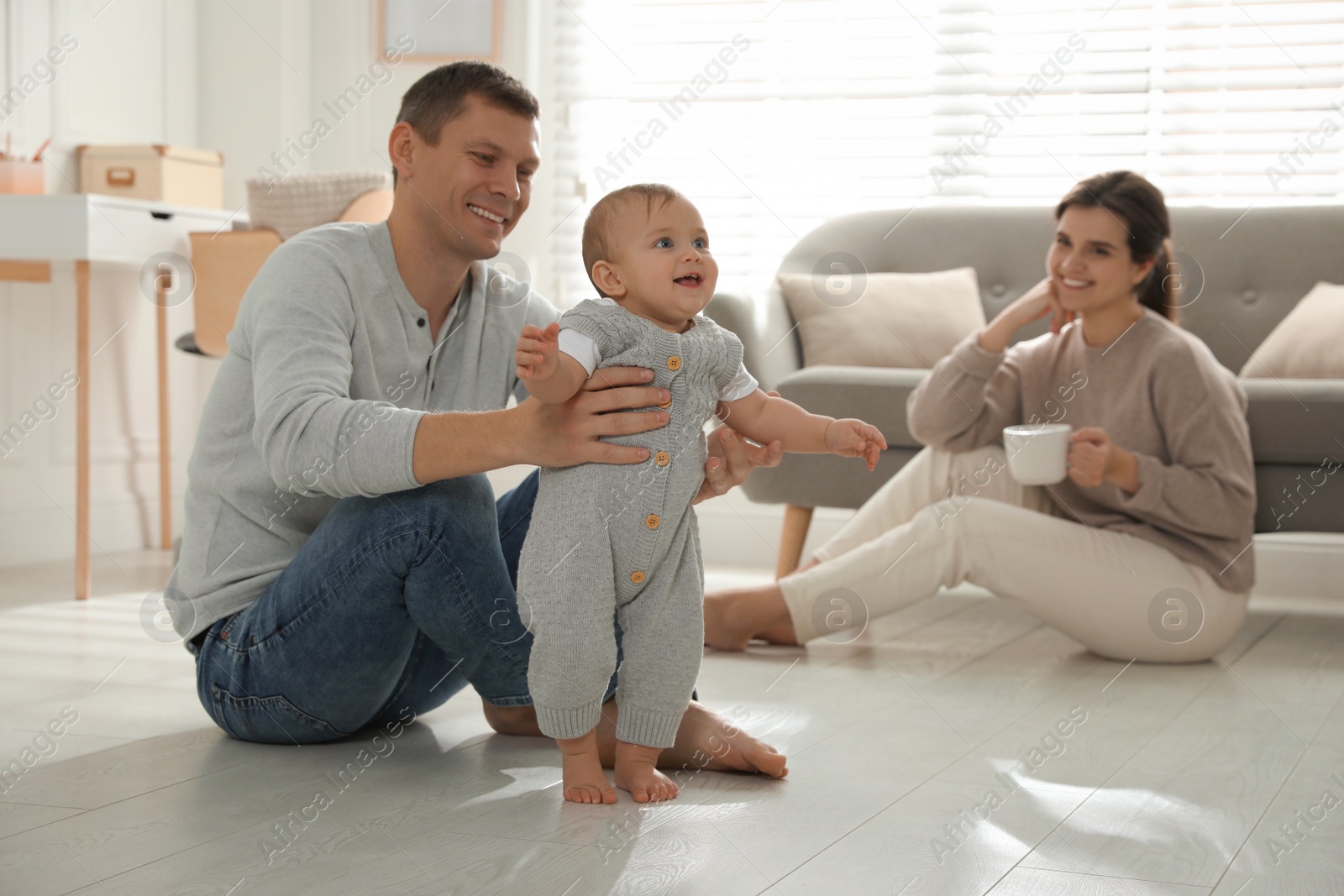 Photo of Father supporting his baby daughter while she learning to walk at home