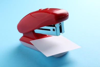 Photo of One new bright stapler with paper note on light blue background, closeup