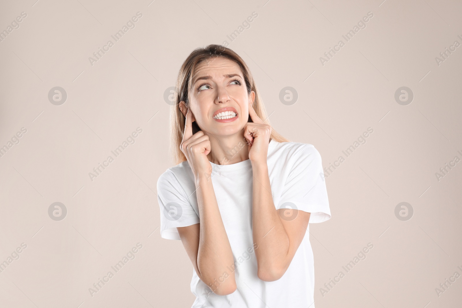 Photo of Emotional young woman covering her ears with fingers on beige background