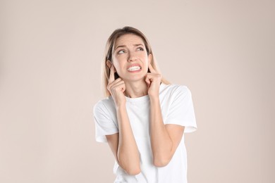 Emotional young woman covering her ears with fingers on beige background