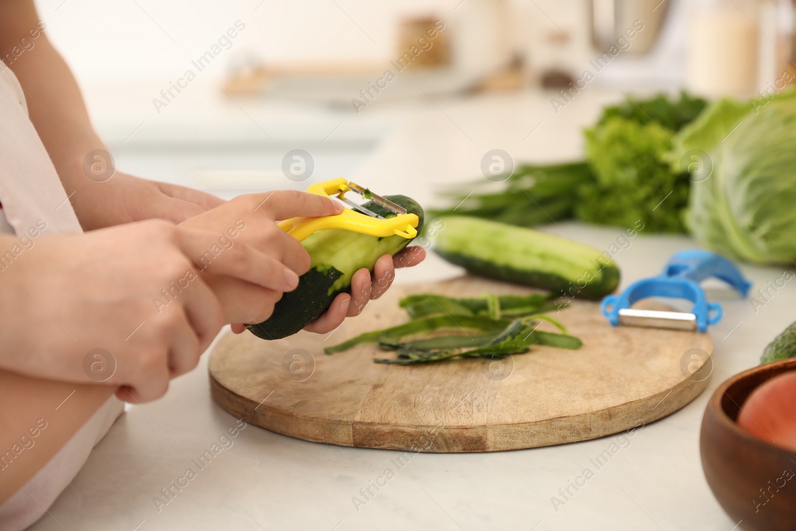 Photo of Mother teaching daughter to peel vegetable at kitchen counter, closeup