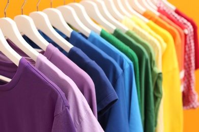 Photo of Rainbow clothes on hangers against color background, closeup