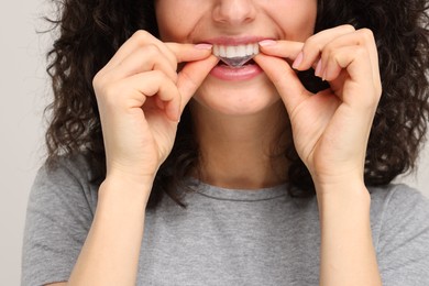 Photo of Young woman applying whitening strip on her teeth against light grey background, closeup