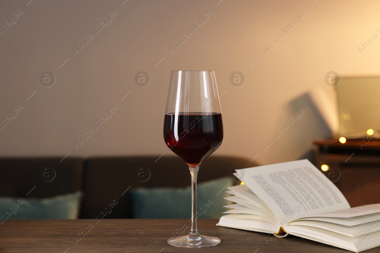Photo of Glass of red wine and open book on wooden table in room. Relax at home