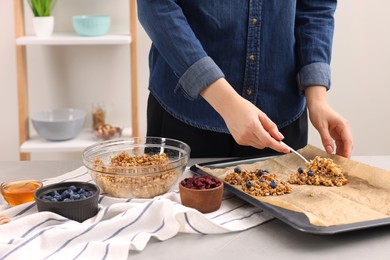 Photo of Making granola bars. Woman putting mixture of oat flakes, dry fruits and other ingredients onto baking tray at table in kitchen, closeup
